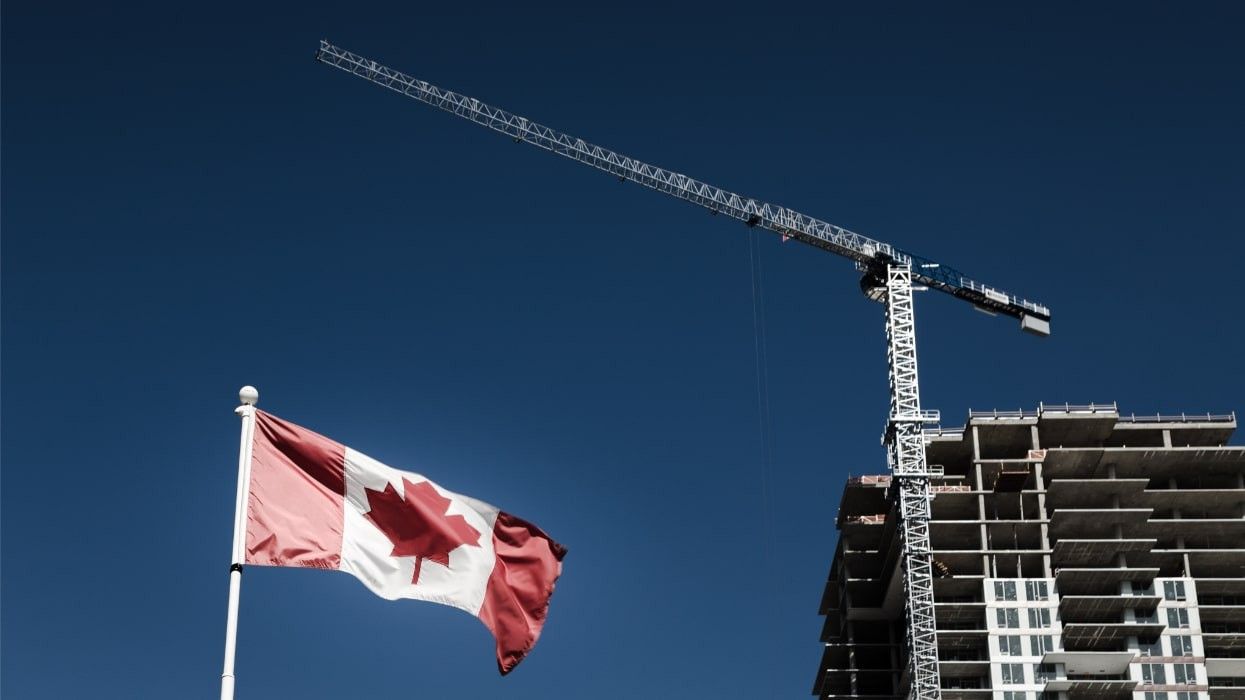 A Canadian flag flying in front of an apartment building under construction.