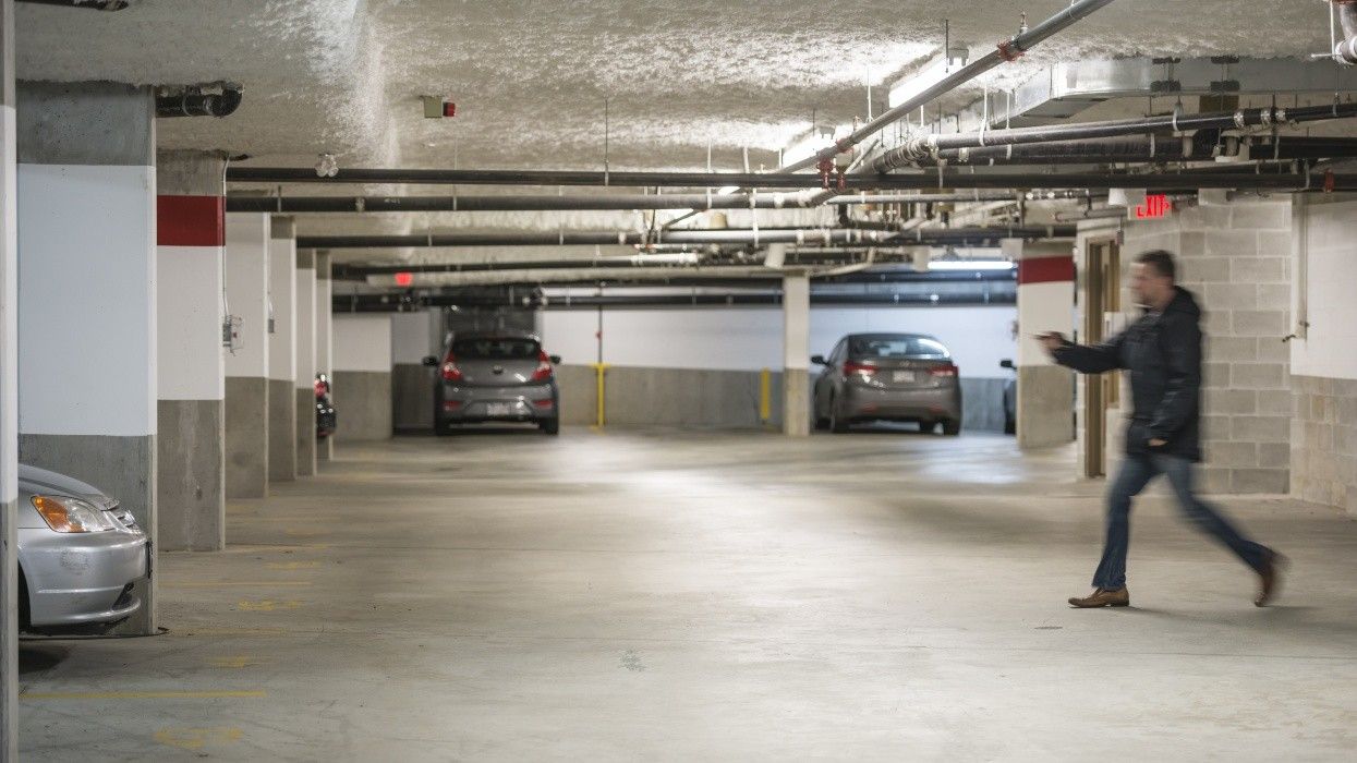 A man walking towards a car in an underground parkade.