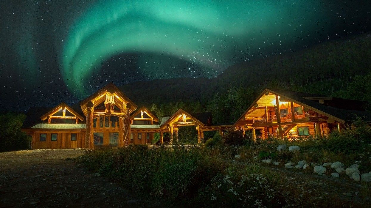 A series of interconnected wooden cabins beneath the northern lights.