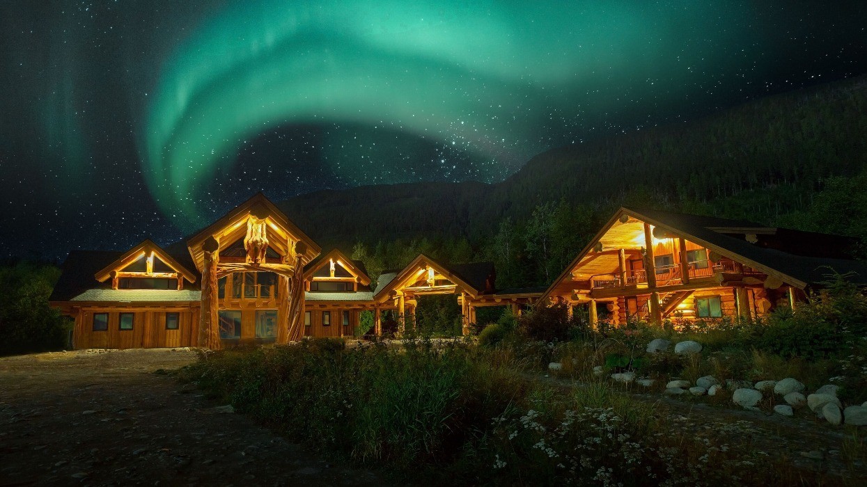 A series of interconnected wooden cabins beneath the northern lights.