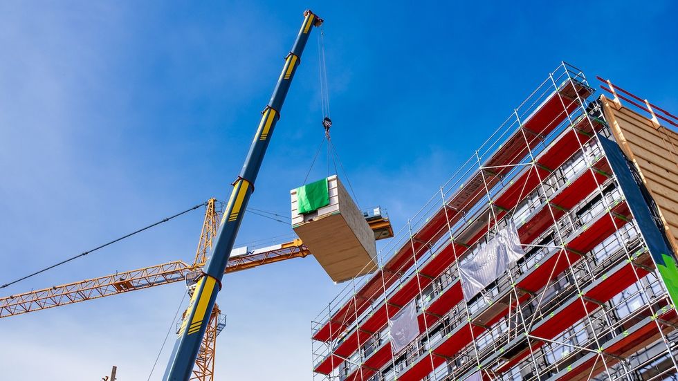 Crane lifting a wooden building module on mid-rise building through prefabricated construction.